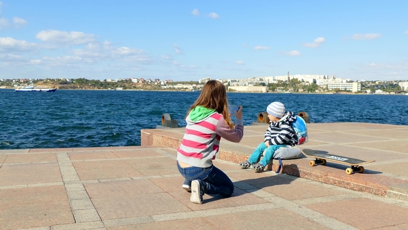 A Girl Takes Pictures of a Child on a Smartphone Near the Sea