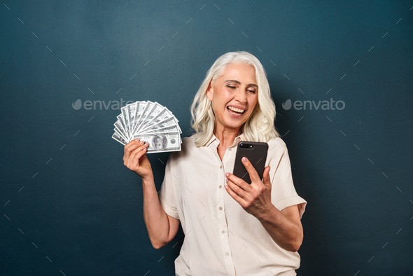 Mature happy old woman holding money using mobile phone. - Stock Photo - Images