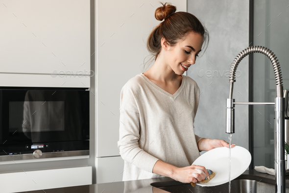 Portrait of a smiling young woman washing dishes Stock Photo by vadymvdrobot
