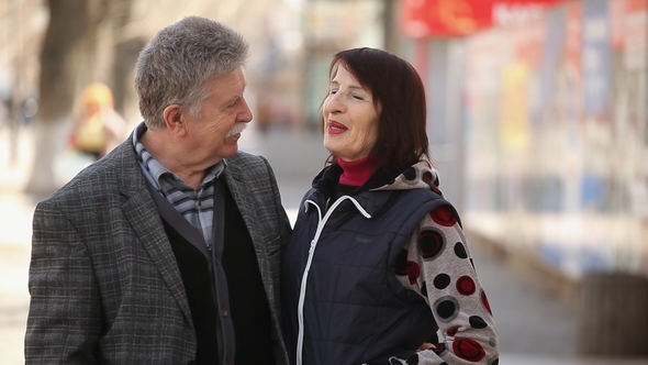 A Cheery Senior Couple Embraces Each Other and Talks on a City Street in Spring