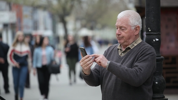 A Senior Man Browsing the Net on His Smartphone in a City Street in Spring