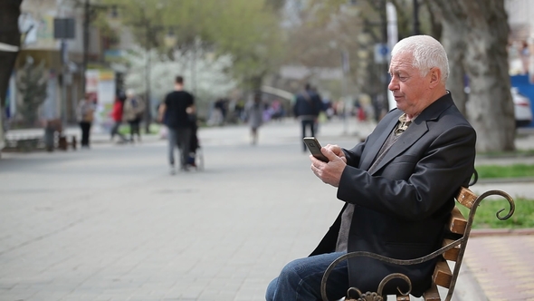 A Grey-headed Man Browsing the Net on His Mobile in a City Street in Spring