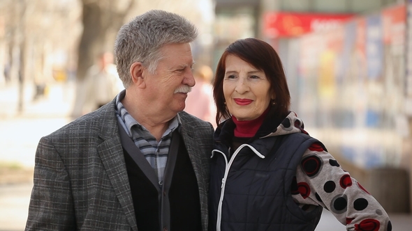 A Happy Senior Couple Embraces Each Other and Smiles on a City Street in Spring