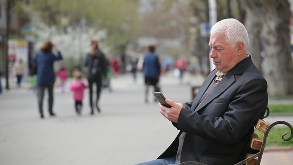 White-headed Man Surfing the Net on His Mobile in a City Street in Spring