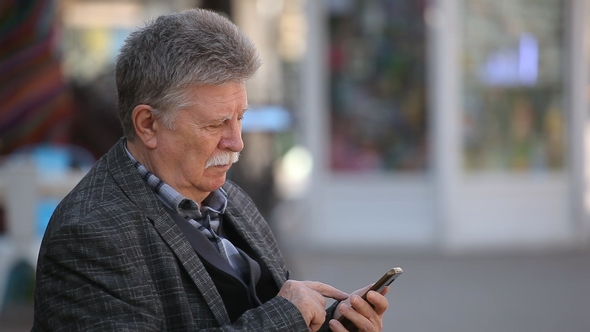 A Smart Old Man Logs on the Web on His Mobile in a City Street in Spring