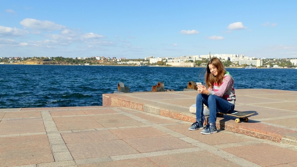 The Girl Sits on the Quay and Makes Selfie