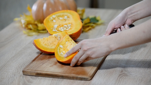 Woman Cleaning Pumpkin on Wooden Kitchen Table. Male Preparing To Cutting Orange Pumpkin Piece. alt