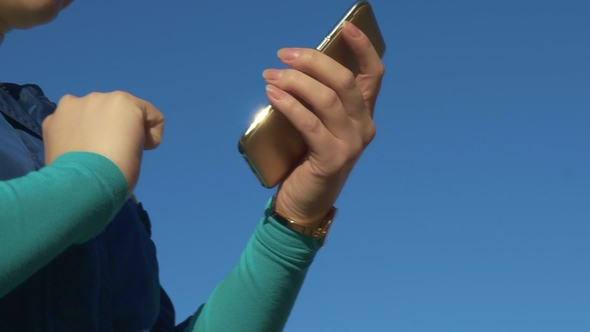 Young Woman Browsing the Internet on the Phone and Chatting Outdoors