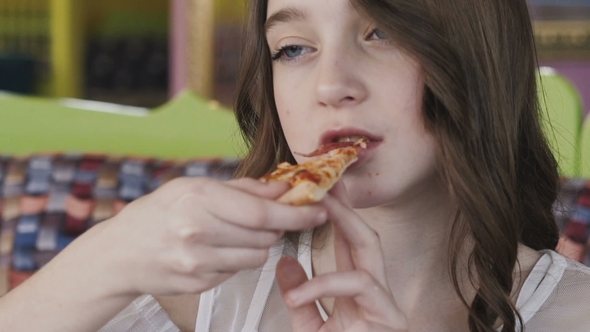 Portrait Of Pretty Young Girl Eating Pizza In Cafe By MAXIMUMSTOCK