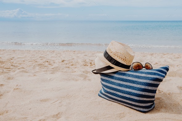 Summer beach bag and accessories - straw hat, flip flops and sunglasses on sandy  beach and azure sea on background, Stock image