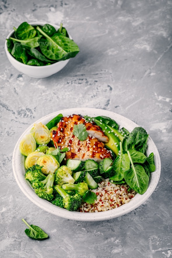 Healthy bowl with grilled chicken, quinoa, spinach, avocado, brussels sprouts, broccoli, cucumbers Stock Photo by nblxer