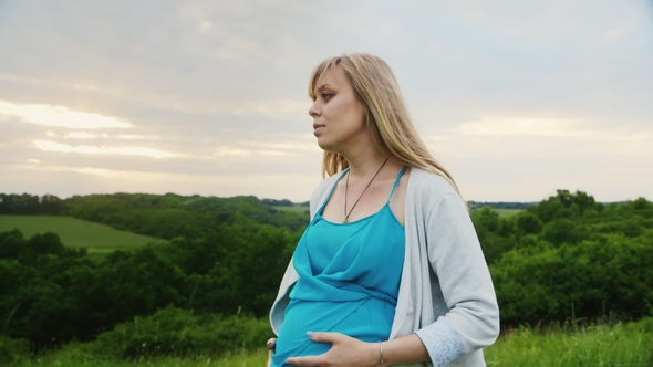 Pregnant Woman Walking in the Scenic Bridge on a Background of Green Forest alt