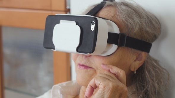 of Senior Woman Is Sitting On The Couch And Putting On VR Glasses With Cellphone. Good-looking alt