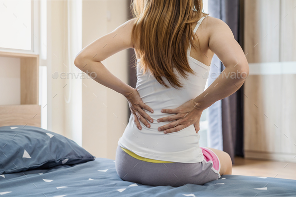 Woman suffering from back ache on the bed Stock Photo by kitzstocker