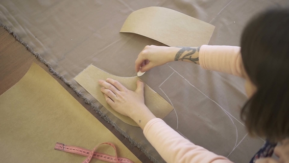 Female Fashion Designer Is Delineating Details of Dress on the Grey Cloth in Her Studio. alt
