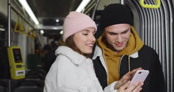 Crop View of Cheerful Couple Talking and Smiling While Looking at Smartphone Screen. Millennilal alt