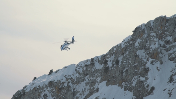 The Helicopter Flies Against the Background of a Rocky Snow-capped Mountain alt