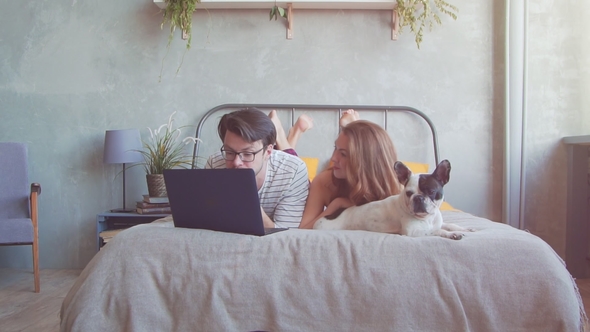 Happy Young Couple with French Dog with Laptop at Home.
