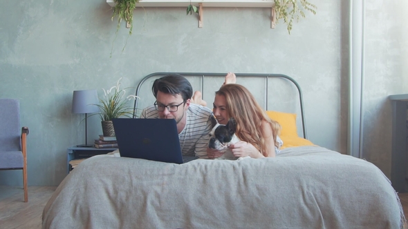 Happy Young Couple with French Dog with Laptop at Home