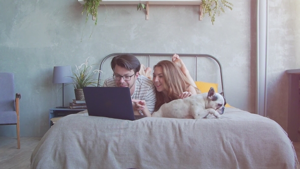Happy Young Couple with French Dog with Laptop at Home.
