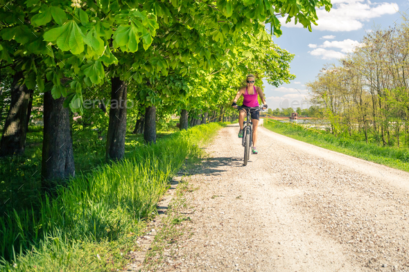 Woman cycling a mountain bike in city park, summer day Stock Photo by blas