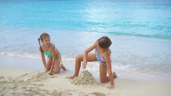 Two Little Happy Girls Have a Lot of Fun at Tropical Beach Playing Together with Sand alt