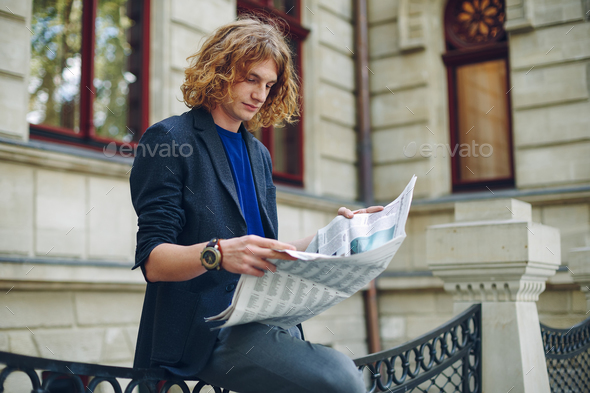 Young reddish man reading newspaper near old style building - Stock Photo - Images