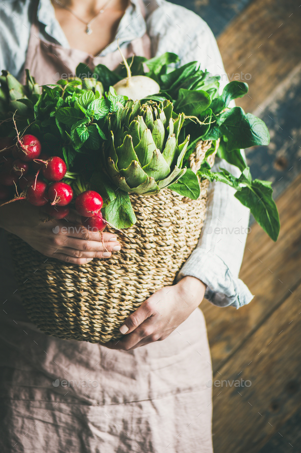Female farmer in apron holding basket with fresh vegetables - Stock Photo - Images