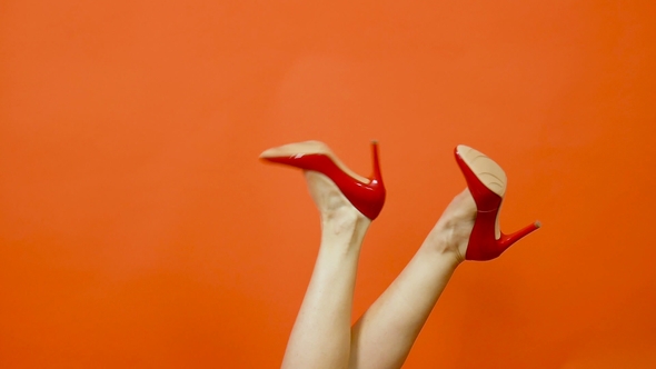 Sexy Woman's Legs in Red High Heels on a Bright Orange Background. They Swing From Side To Side