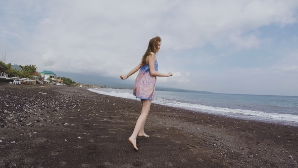 Young Girl in a Beautiful Dress Runs and Looks Around the Black Beach of Volcanic Sand in Bali