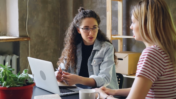 Young Enterpreneur Is Talking To Her Partner in Modern Office While Sitting at Desk Together. Women alt