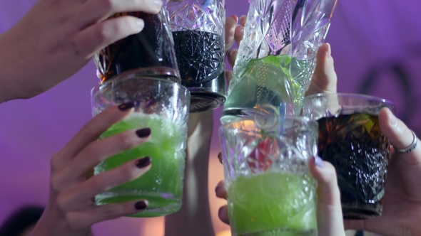 People's Hands Make Toast with Glasses with Alcoholic Multi-colored Cocktails at Club alt