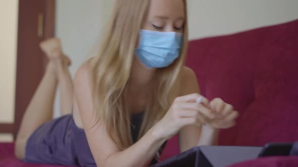 A Young Woman Wearing a Medical Face Mask Works From Home During Coronavirus Self-isolation. Self alt