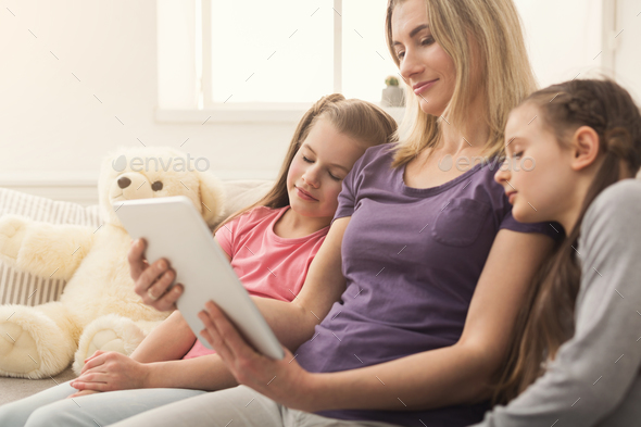 Happy beautiful woman using digital tablet and her daughters sleeping Stock Photo by Milkosx