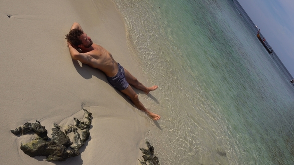 Relaxing Man Lying on White Beach Sand Washed with Warm Azure Ocean Water