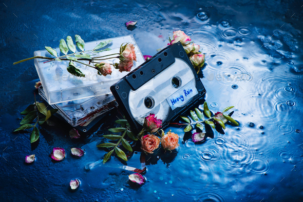 Audio cassette tape with Heavy Rain label in a scene with rose petals and raindrops. Melancholy