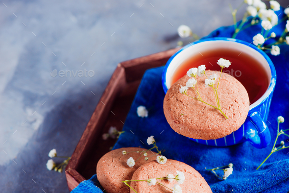Morning scene with a small blue teacup and oatmeal cookies on a wooden tray with a blue linen napkin