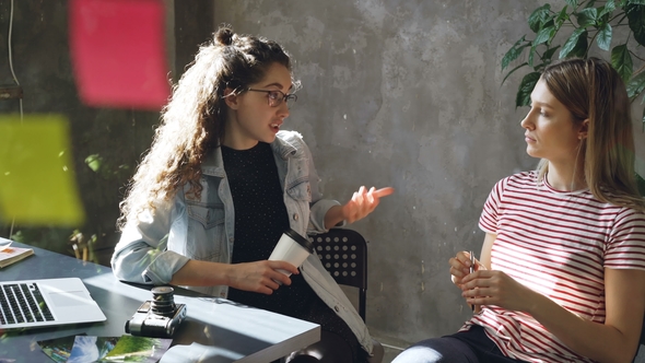 Young Female Colleagues Are Sitting at Desk Sharing Ideas in Modern Office. Glassboard with alt