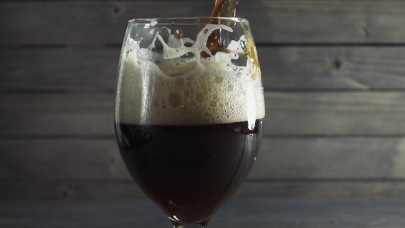 Pouring Cold Dark Beer Into a Glass. Over Dark Wooden Background.