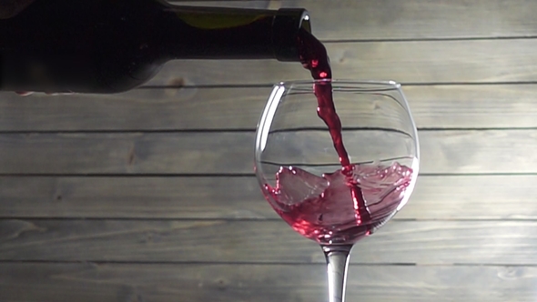 Pouring Red Wine Into the Glass Against Wooden Background.