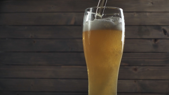 Beer Poured in Glass on Wood Background. Foam Sliding Down Side.
