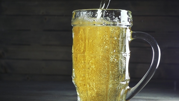 Shot of Pouring Beer Into Beer Mug. Over Dark Wooden Background