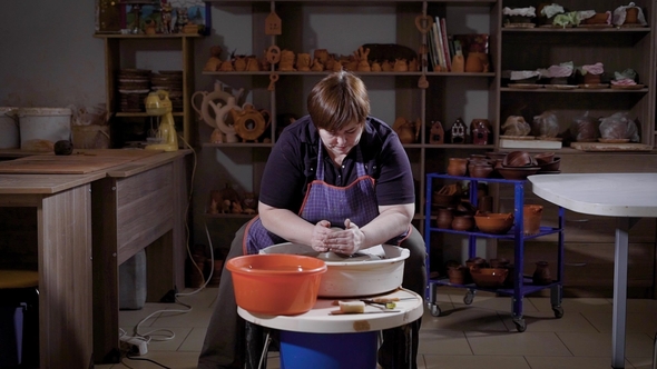 an Adult Woman Is Engaged in Creating a Vase of Clay, She Sits Behind a Potter's Wheel and Forms alt