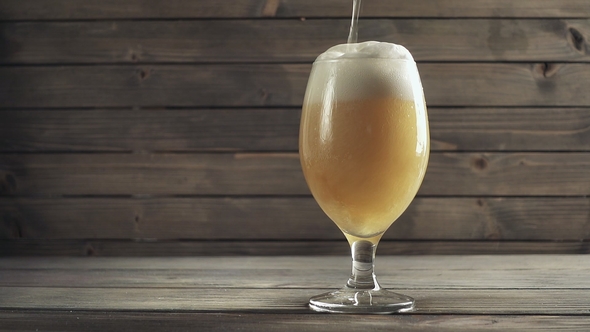 Beer Poured in Glass on Wood Background. Foam Sliding Down Side