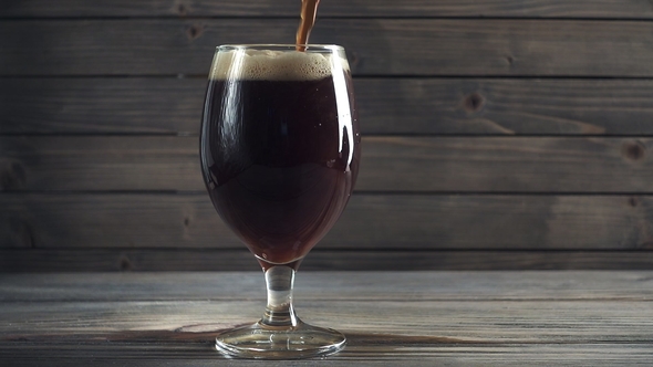 Pouring Cold Dark Beer Into a Glass. Over Dark Wooden Background.