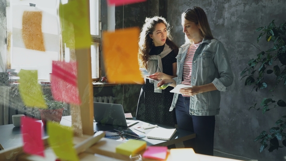 Cheerful Designers Are Standing Near Table and Choosing Photos for Project. Young Women Are Having alt