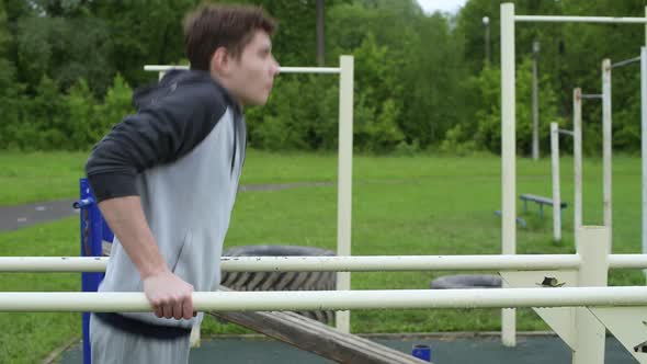 Side view of a training guy. teenager push ups on uneven bars alt