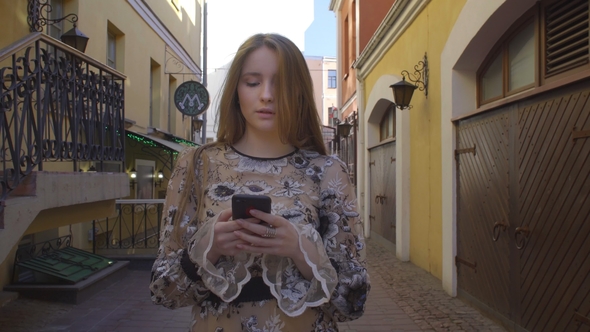 Young Girl Walking Down the Street with a Phone in Hands