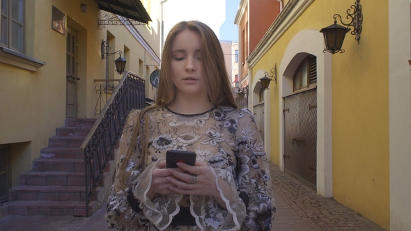 Young Girl Walking Down the Street with a Phone in Hands