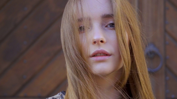 of a Girl with Long Wheat-colored Hair. Looks Directly Into the Camera, the Hair Develops the Wind